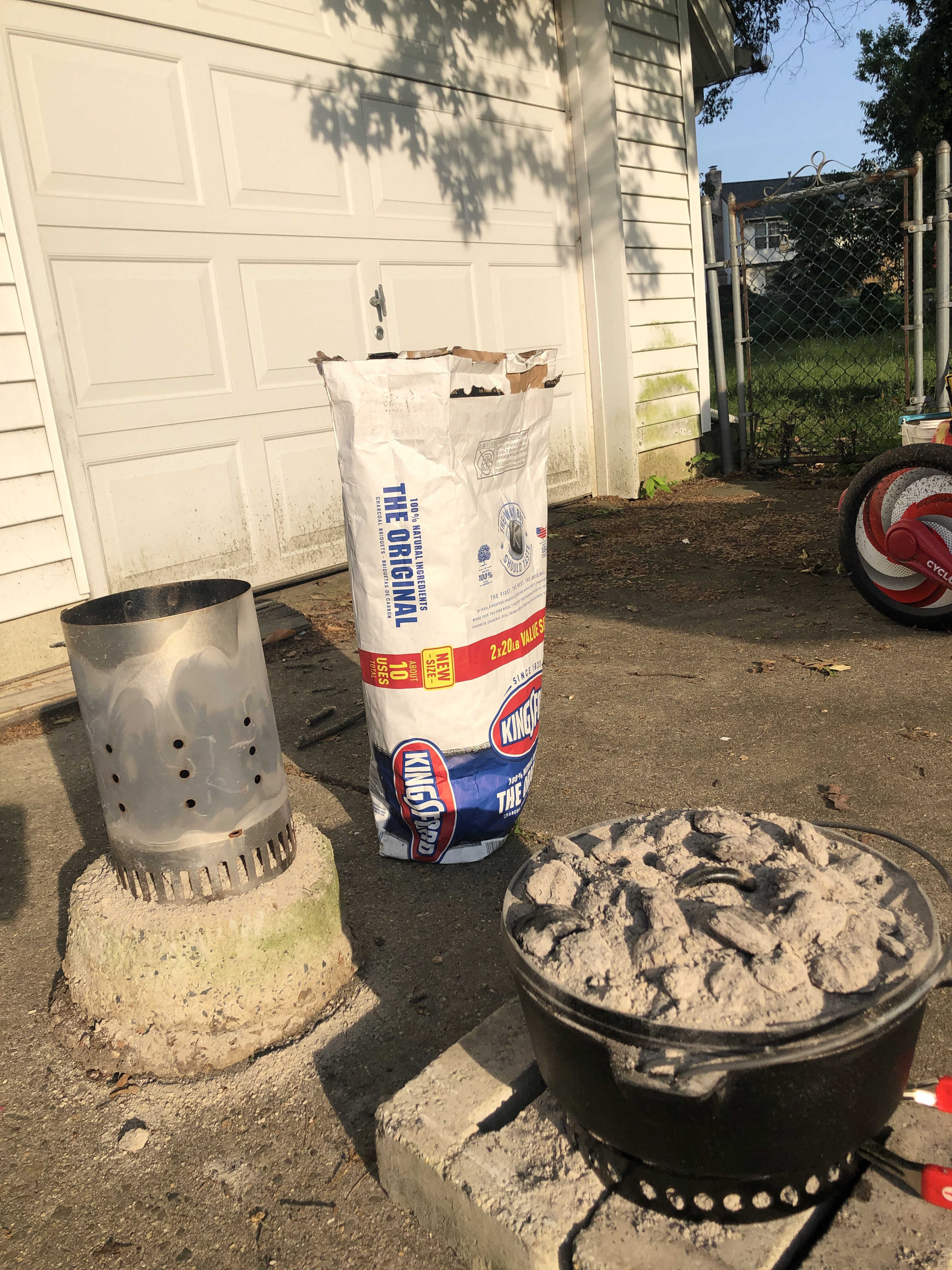 Dutch oven, charcoal chimney, bag of charcoal on driveway 